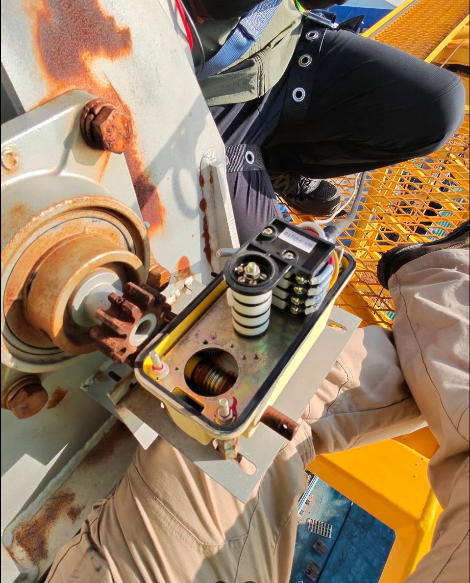 Electrician servicing a limit switch enclosure on elevated yellow industrial equipment